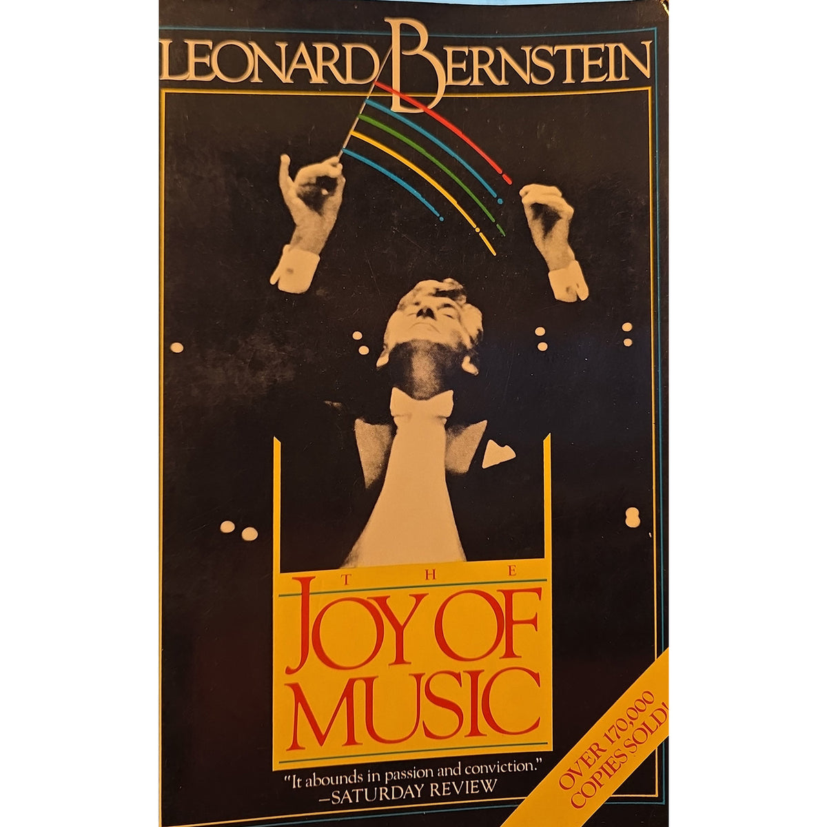 The front cover of the book 'The Joy of Music' by Leonard Bernstein, featuring a black background with a stylized illustration of a conductor and gold and red typography.