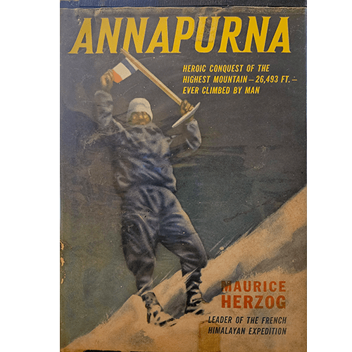 Dust jacket of Annapurna by Maurice Herzog featuring a triumphant mountaineer waving a flag atop a snowy Himalayan summit.