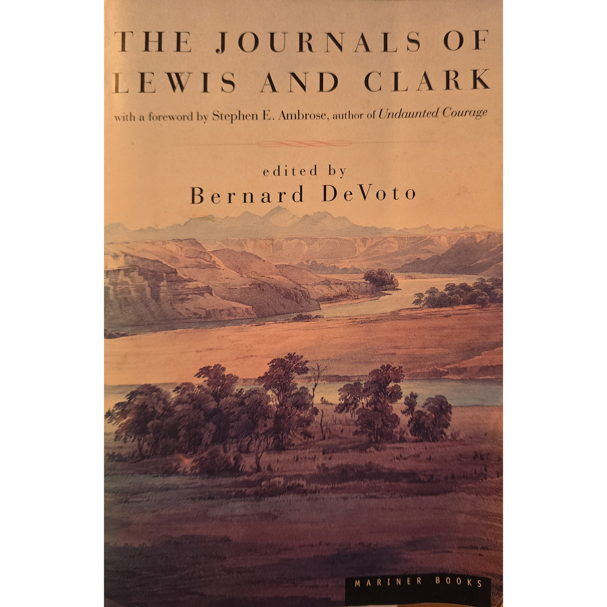 Book cover of 'The Journals of Lewis and Clark' edited by Bernard DeVoto, featuring a sepia-toned landscape illustration with mountains, trees, and a river. The Mariner Books logo is visible at the bottom.