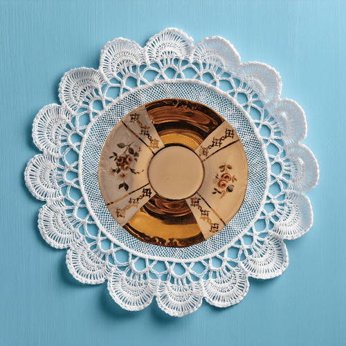 Decorative white lace doily with a vintage teacup design on a blue background