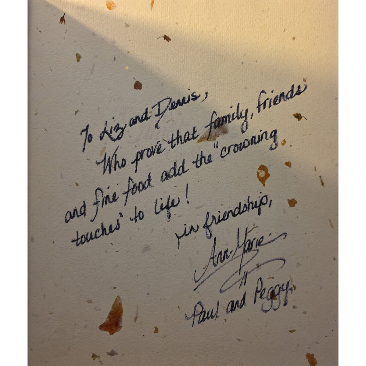 innterior book pagefeaturing a handwritten black ink message and signatures. The item is shown under warm, direct sunlight casting a shadow across the top-left corner.