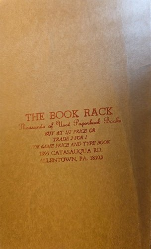 A close-up of a brown paper book bag with red printed text reading 'THE BOOK RACK' and smaller text below, photographed against a matching brown background.