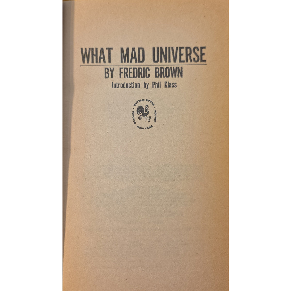 A book cover for 'What Mad Universe' by Fredric Brown, featuring a tan paper background with black printed text and a small circular logo near the bottom center.