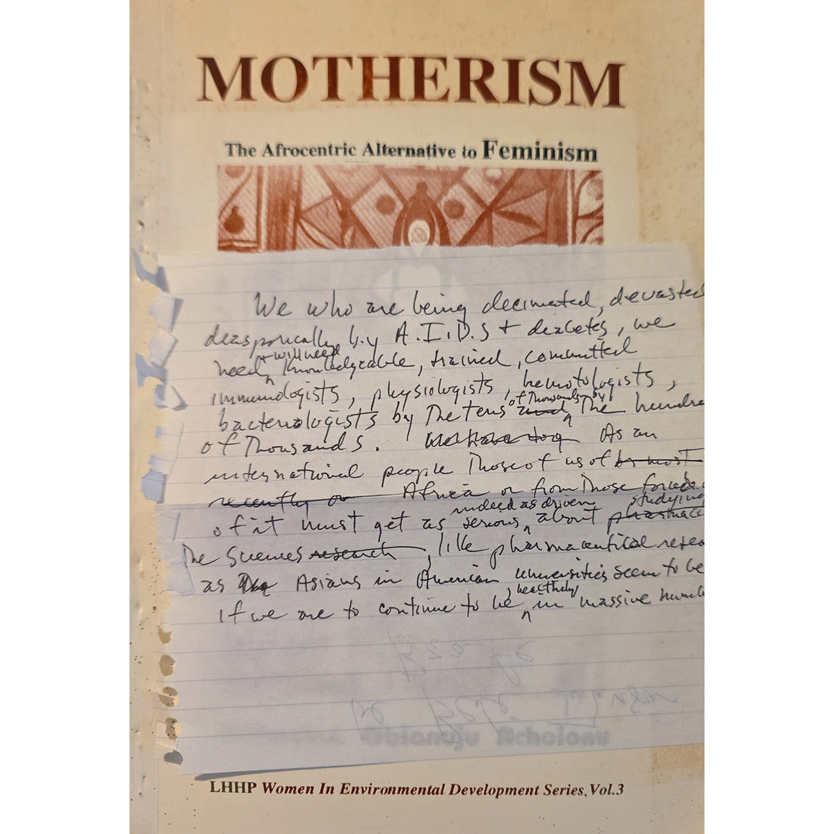 A book or booklet cover titled "MOTHERISM" with the subtitle "The Afrocentric Alternative to Feminism," showing a beige cover with a printed pattern near the top and a large handwritten note overlaid across the center. Small text at the bottom reads "LHHP Women In Environmental Development Series, Vol.