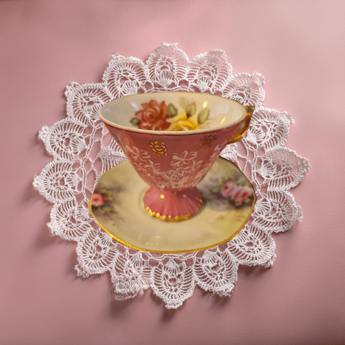 Vintage-style teacup with floral design on a lace doily against a pink background