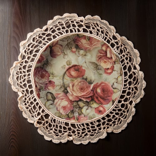 Decorative saucer with floral design and lace-like edge on a dark wooden surface