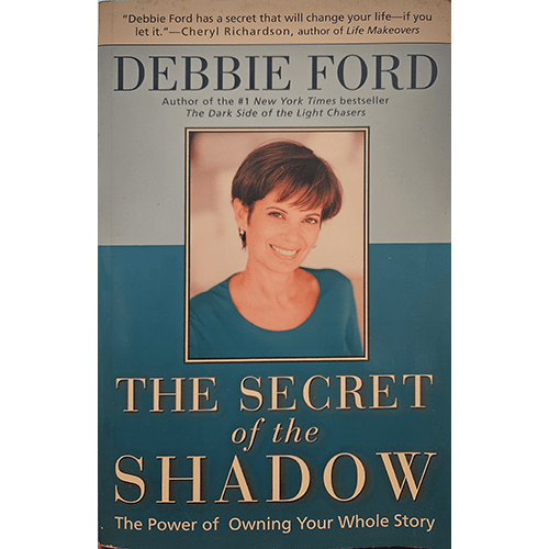 Book cover of The Secret of the Shadow by Debbie Ford, featuring a portrait of the author with a soft smile, a light blue background, and bold white and yellow text outlining the title and subtitle.