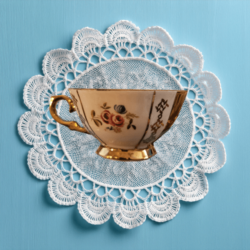 Teacup with floral design on a lace doily against a blue background