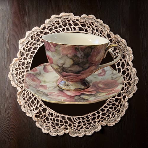 Floral teacup and saucer on a lace doily against a dark wooden background