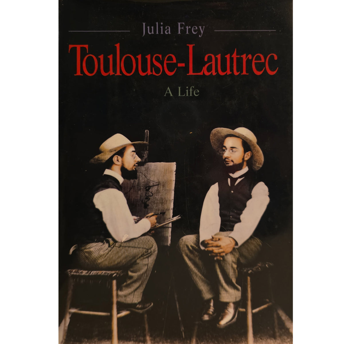 Book cover for 'Toulouse-Lautrec: A Life' by Julia Frey, featuring a dark background with the title in red and a sepia-toned photograph of two men seated and drawing or talking.