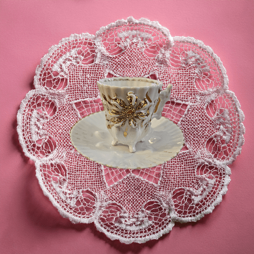 Decorative teacup with lace doily on a pink background