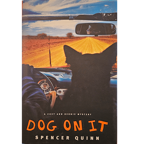 Cover of Dog On It by Spencer Quinn, featuring a dog and a driver on an open road, viewed from inside a car. A suspenseful Chet and Bernie mystery.