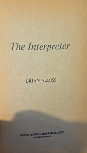 A close-up of a book cover or printed page with the title 'The Interpreter' and author name 'Brian Aldiss' on a warm beige background. A dark shadow falls across the lower portion, and 'New English Library' is printed at the bottom.