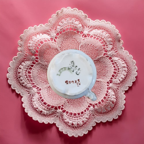 Cup of coffee on a lace doily with a pink background