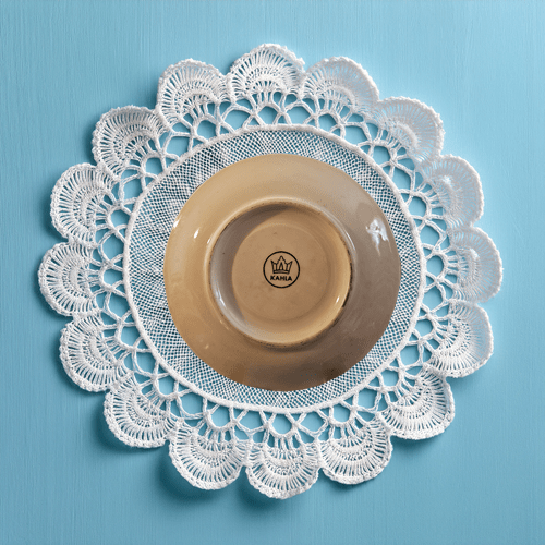 White lace doily with a beige saucer on a blue background