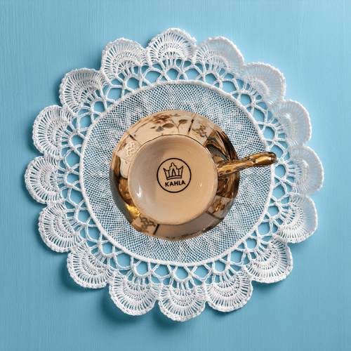 Café au lait cup with gold handle on a lace doily against a blue background
