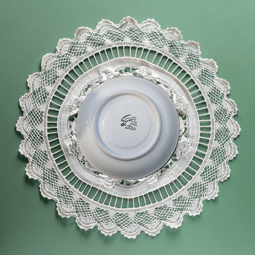 White lace doily on a green background with a white bowl underneath