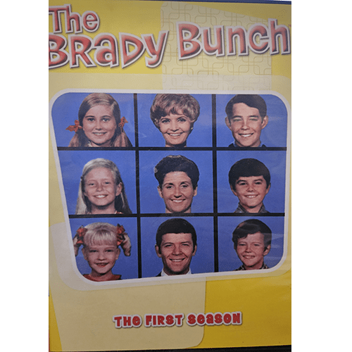 DVD cover of The Brady Bunch: The First Season featuring a yellow background and portraits of the nine main characters, including Carol, Mike, and the six Brady children, along with housekeeper Alice.