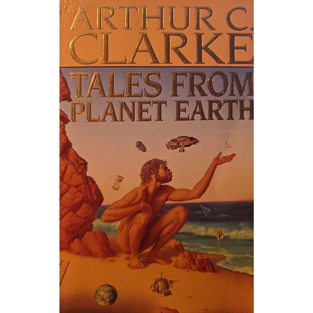 Book cover for 'Tales From Planet Earth' by Arthur C. Clarke, featuring a warm orange and brown sci-fi illustration of a figure on a beach with floating spacecraft and space debris.