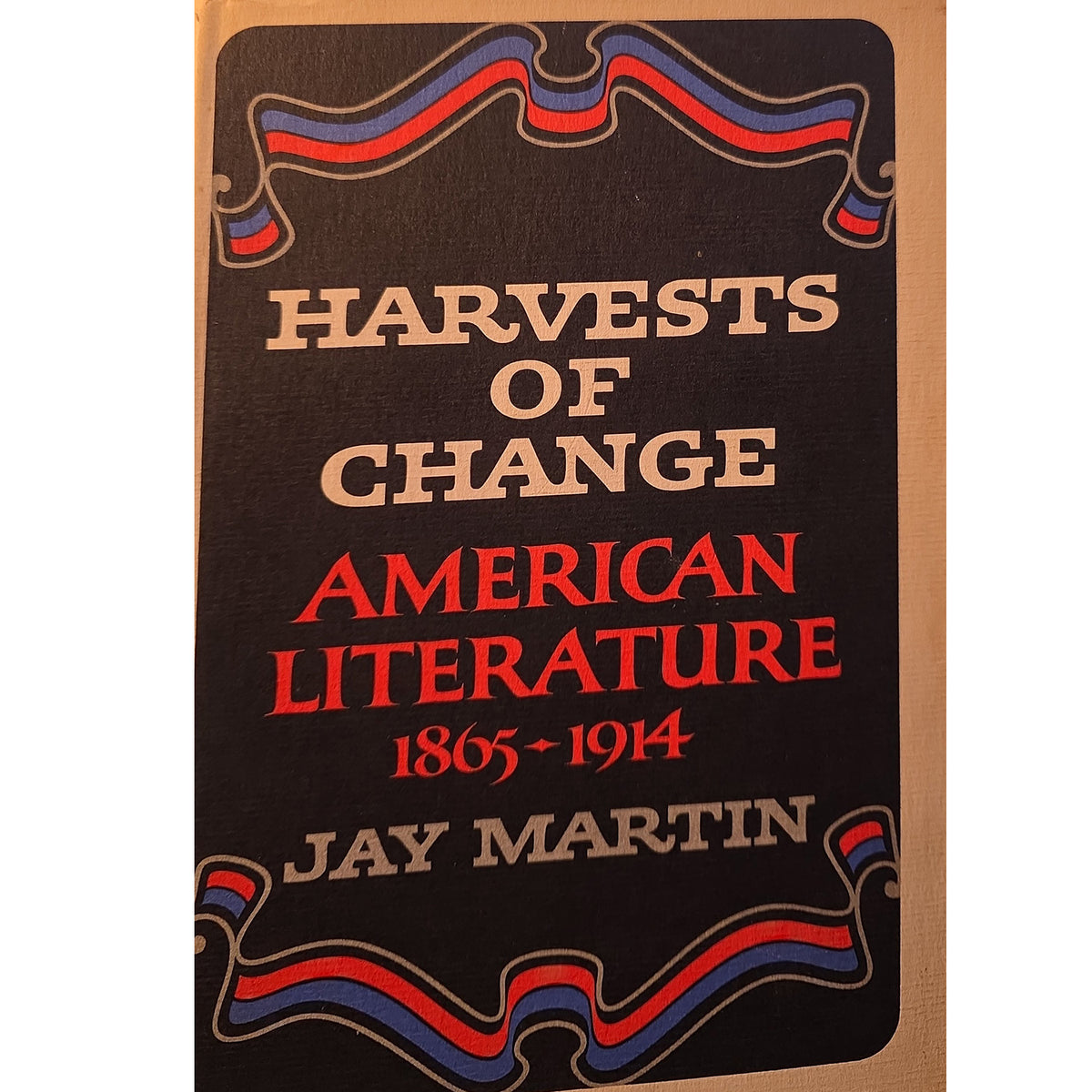 Book cover of 'Harvests of Change: American Literature 1865-1914' by Jay Martin, featuring a black background with red and beige text and decorative red, blue, and beige ribbon motifs.