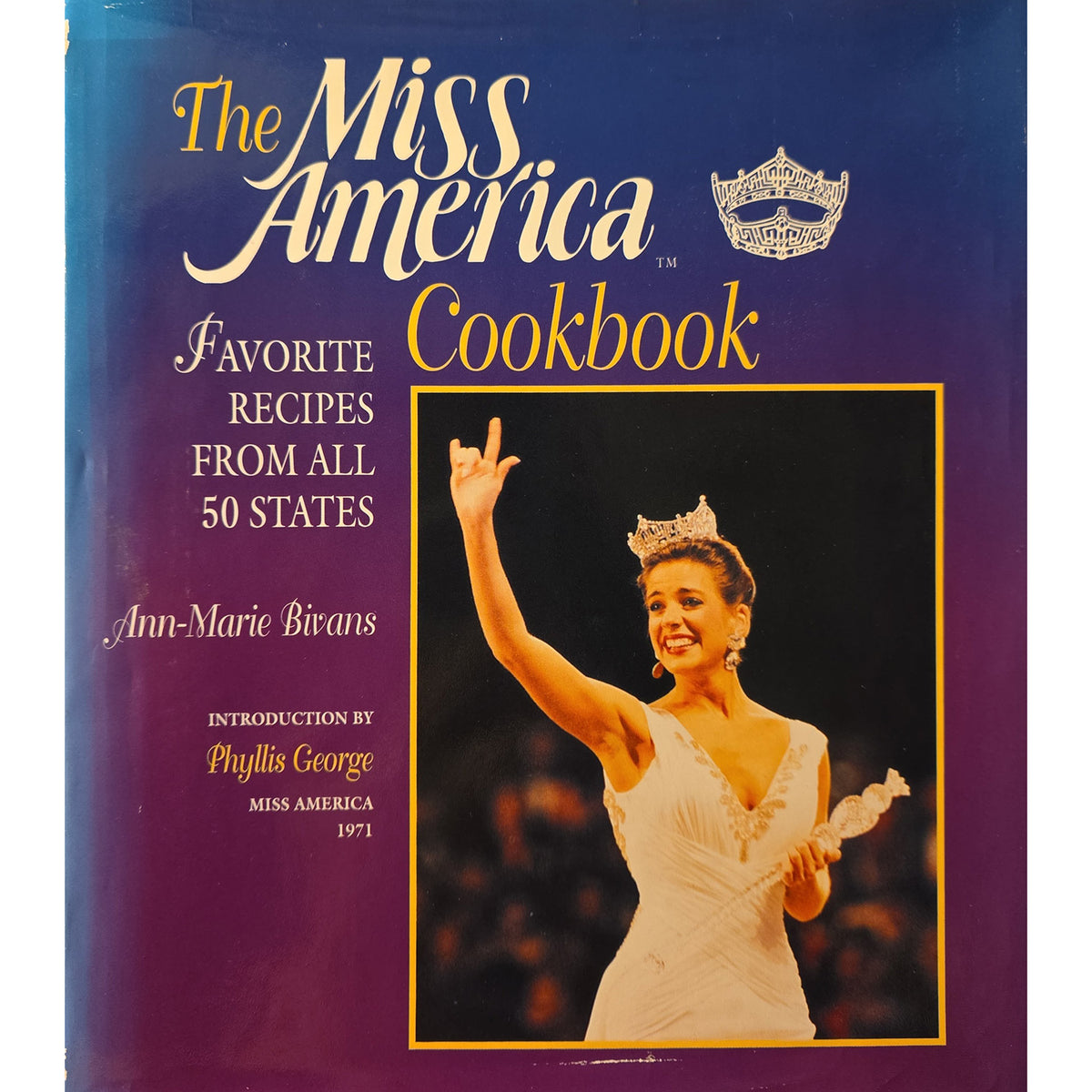 The Miss America Cookbook book cover, featuring a blue-to-purple gradient background with gold and white typography and a central photo of a crowned Miss America in a white gown raising her hand.