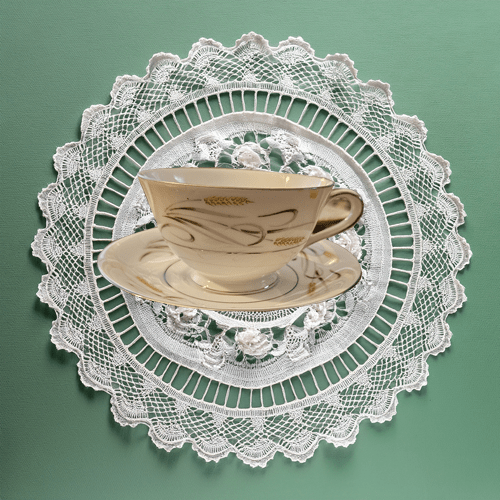 Teacup and saucer on a lace doily against a green background