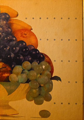 A close-up of a still life painting featuring dark purple and green grapes, orange, and yellow fruit on a warm gold background with small evenly spaced dots.