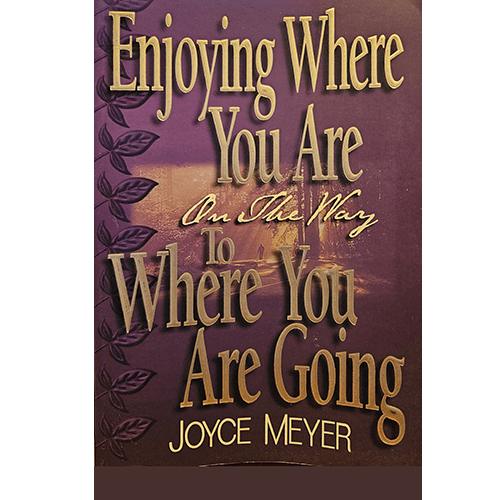 The cover of Joyce Meyer's "Enjoying Where You Are On The Way To Where You Are Going" features gold, embossed lettering on a purple background, with leaf accents and a calming, soft glow in the distance.