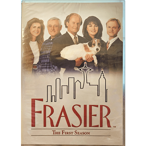 The cover of Frasier: The First Season DVD features Frasier Crane holding Eddie the dog, with family members Martin, Niles, Daphne, and Roz, set against a Seattle skyline, promising laughs and warmth.