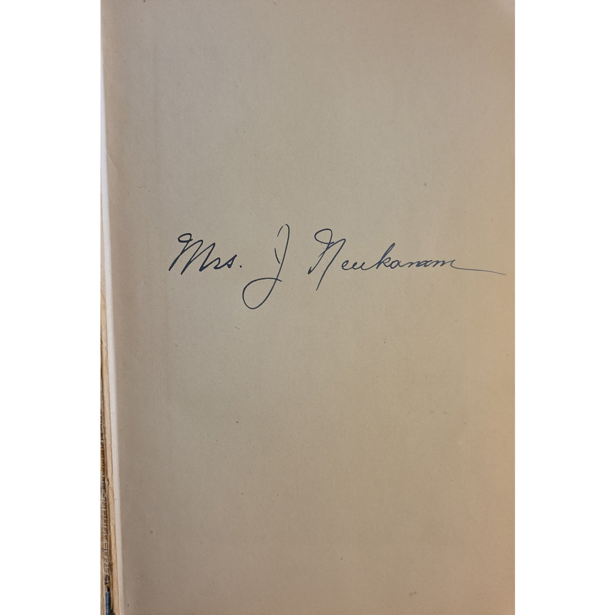 A close-up of a beige book page featuring a dark blue handwritten signature that reads 'Mrs. J. Neukomm'.