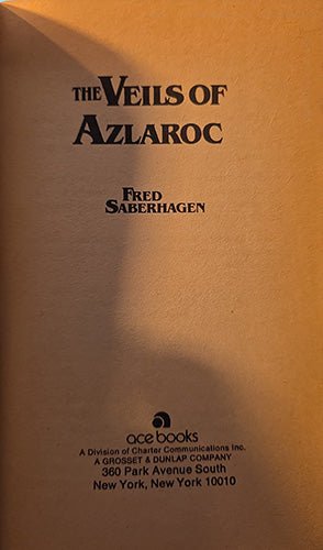 The half title of the book 'The Veils of Azlaroc' by Fred Saberhagen, published by Ace Books. The cover is a warm tan or light brown color with black text, photographed under warm, directional lighting that casts a shadow on the left side.