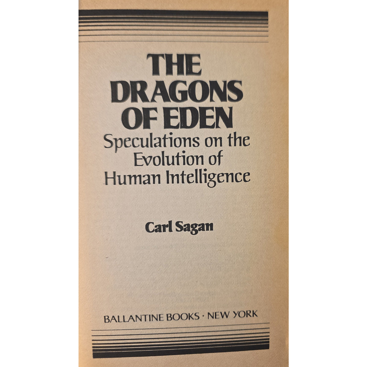 half title of the book 'The Dragons of Eden: Speculations on the Evolution of Human Intelligence' by Carl Sagan, published by Ballantine Books. The cover is a warm tan/beige color with black text and decorative horizontal lines at the top and bottom.