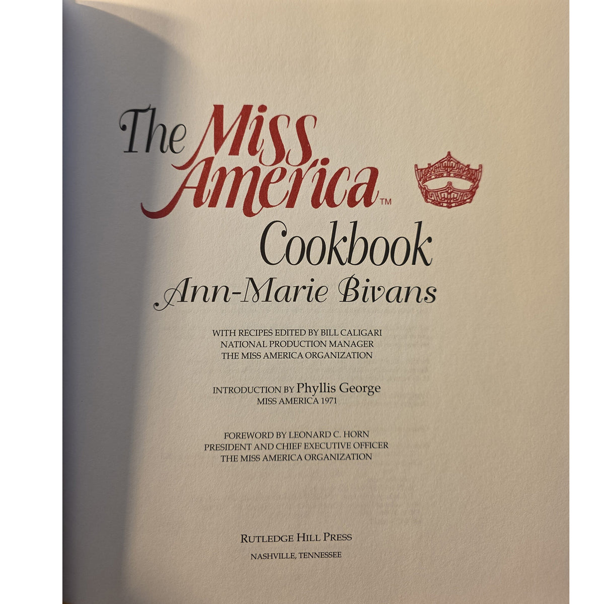 half titleof The Miss America Cookbook by Ann-Marie Bivans, showing a beige cover with red and black typography and a small red crown emblem.