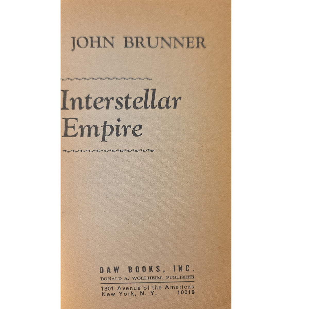 half title page of the book 'Interstellar Empire' by John Brunner, published by Daw Books, Inc., featuring a tan paper background with black printed text.