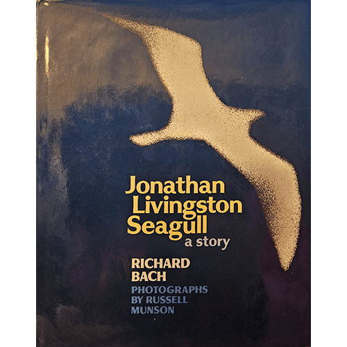 The cover of Jonathan Livingston Seagull by Richard Bach features a striking image of a white seagull silhouette in flight against a deep blue background, symbolizing freedom and aspiration.