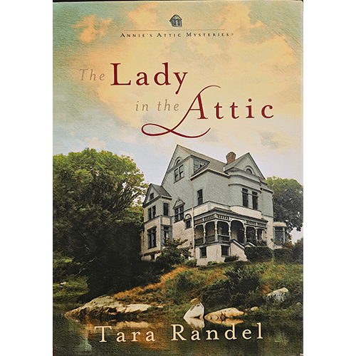 Cover of The Lady in the Attic by Tara Randel, featuring a Victorian-style house perched on a hill surrounded by greenery and rocks. A sky of soft golden hues evokes mystery and nostalgia.