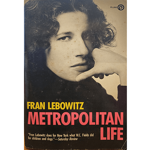 Cover of Fran Lebowitz's "Metropolitan Life," featuring a black-and-white photo of Lebowitz with a contemplative expression, resting her chin on her hand. The title is in bold red letters below her name.