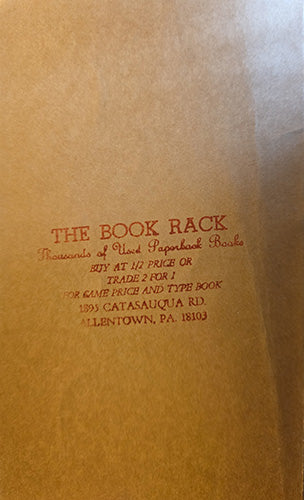 A close-up of a brown paper book bag with red printed text reading 'THE BOOK RACK' and smaller text below, photographed against a matching brown background.