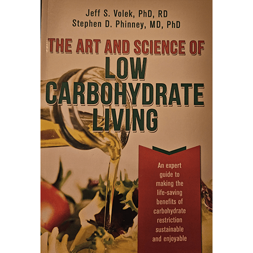 Cover of The Art and Science of Low Carbohydrate Living by Jeff S. Volek and Stephen D. Phinney, featuring a pouring olive oil bottle with vegetables, emphasizing low-carb eating and health benefits.