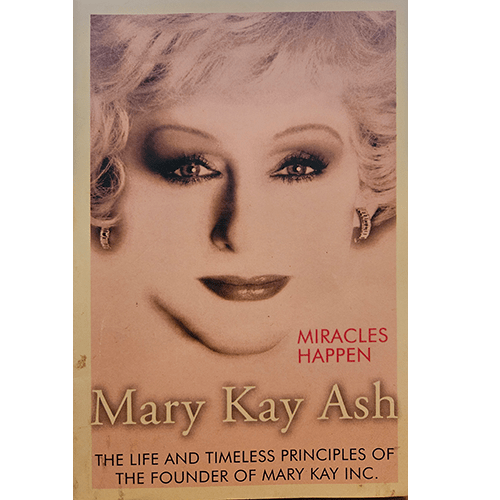 The cover of "Mary Kay Ash: Miracles Happen" features a portrait of Mary Kay Ash in a vibrant, empowering pose, set against a soft pink background, symbolizing her legacy of beauty and empowerment.