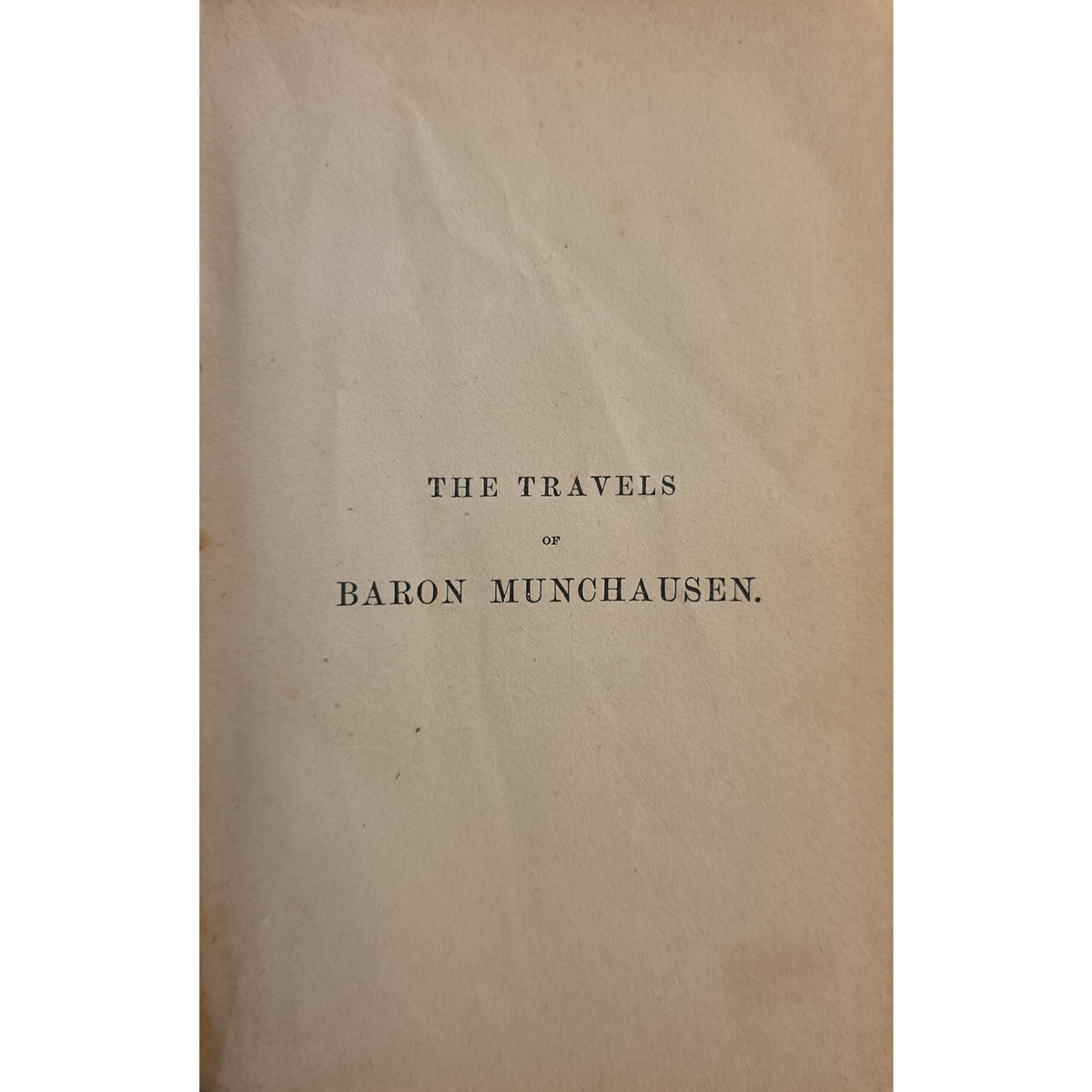 A vintage book or pamphlet cover with a warm beige paper background and black printed text reading 'THE TRAVELS OF BARON MUNCHAUSEN.'.