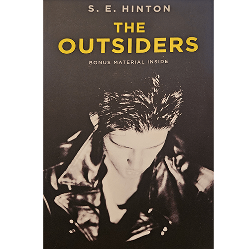  Cover of The Outsiders by S.E. Hinton featuring a black-and-white image of a young man in a leather jacket, with striking yellow title text above. Includes "Bonus Material Inside."