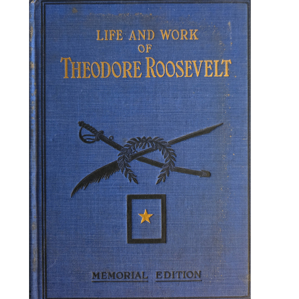 A vintage hardcover book titled 'Life and Work of Theodore Roosevelt' in gold lettering on a textured blue cover, featuring crossed swords and a star emblem, with 'Memorial Edition' printed at the bottom.