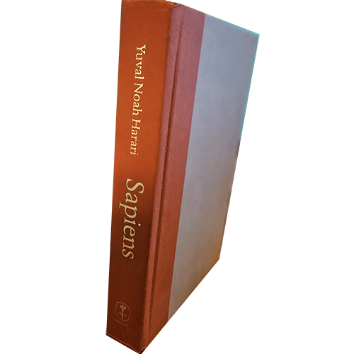 The image shows the hardcover spine of "Sapiens: A Brief History of Humankind" by Yuval Noah Harari, published in 2015. The book's spine is orange with gold lettering and the cover is beige.