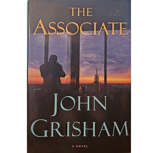 The cover of The Associate by John Grisham shows a silhouette of a man standing in front of tall city skyscrapers at sunset, reflecting the high-stakes world of law and intrigue within the novel.