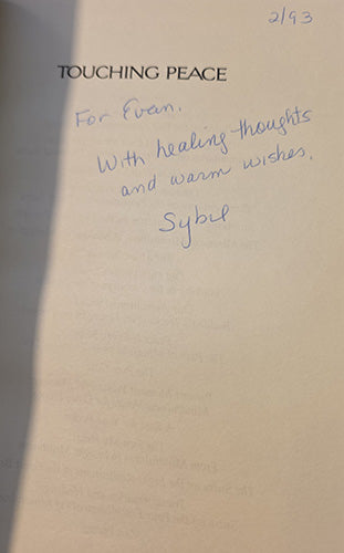 A cream-colored paper card or letterhead with printed black text reading 'TOUCHING PEACE' and a handwritten blue note that says 'For Eve, With healing-thoughts and warm wishes, Sybil' at the bottom right.