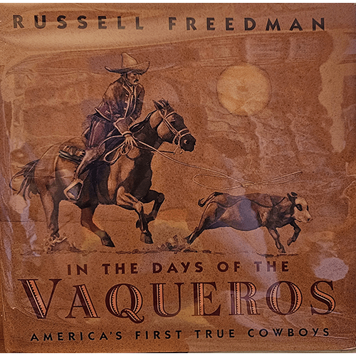 Cover of In the Days of the Vaqueros by Russell Freedman shows a vaquero on horseback roping a steer under a golden sun. The title highlights America's first true cowboys in bold, vintage lettering.