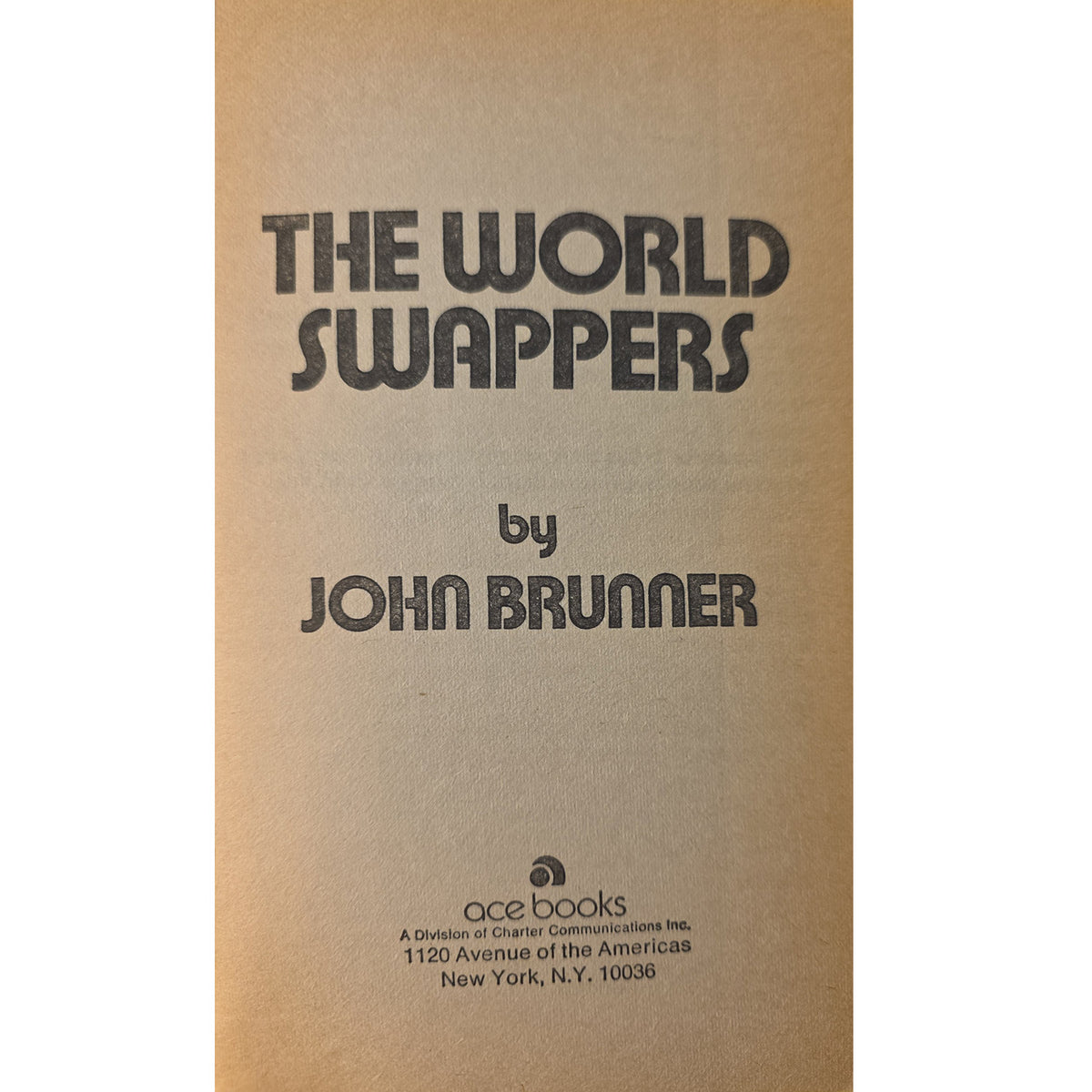 Thehalf titleof the book 'The World Swappers' by John Brunner, published by Ace Books. The cover is a warm tan/kraft paper color with bold black text.