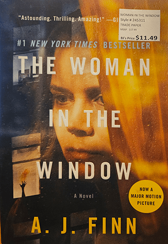 "Cover of 'The Woman in the Window' by A.J. Finn featuring a dark, ominous window with shadows and a faint reflection of a woman's face, symbolizing the suspense and psychological tension of the thriller."