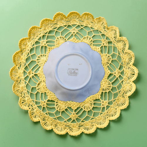 Yellow lace doily with a blue plate underneath on a green background